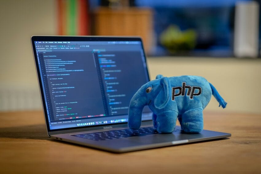 Blue PHP elephant plush on a laptop keyboard in front of a code editor screen