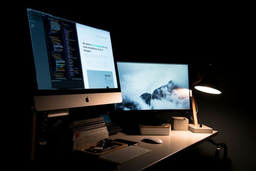 Dual-monitor desk setup with a code editor and a portfolio website on one screen, and a mountain wallpaper on the other
